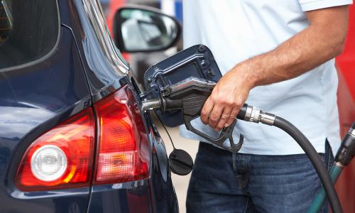 Man in white t-shirt pumping gas into blue car