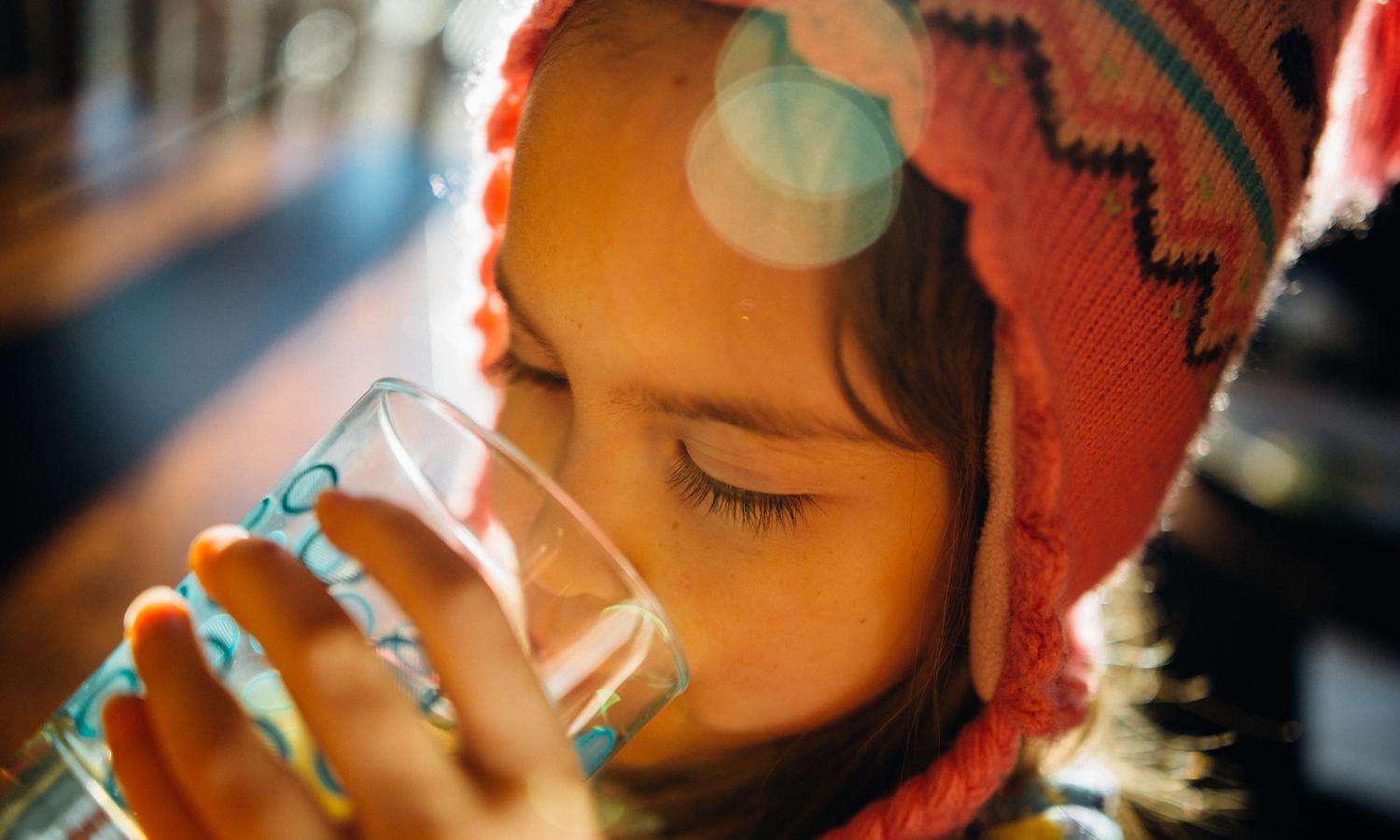 A kid drinks a glass of water.