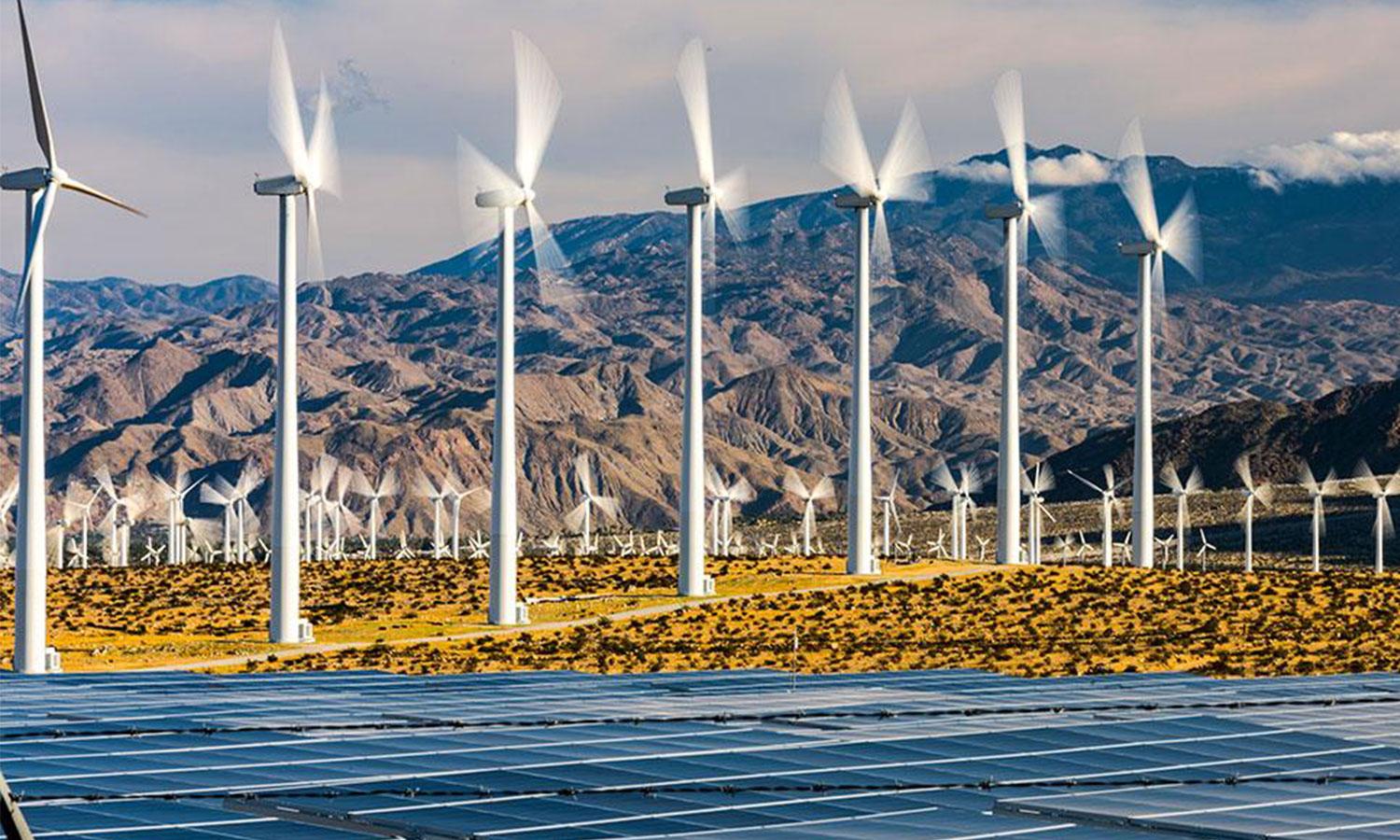 Wind turbines and solar panel array in front of mountain range