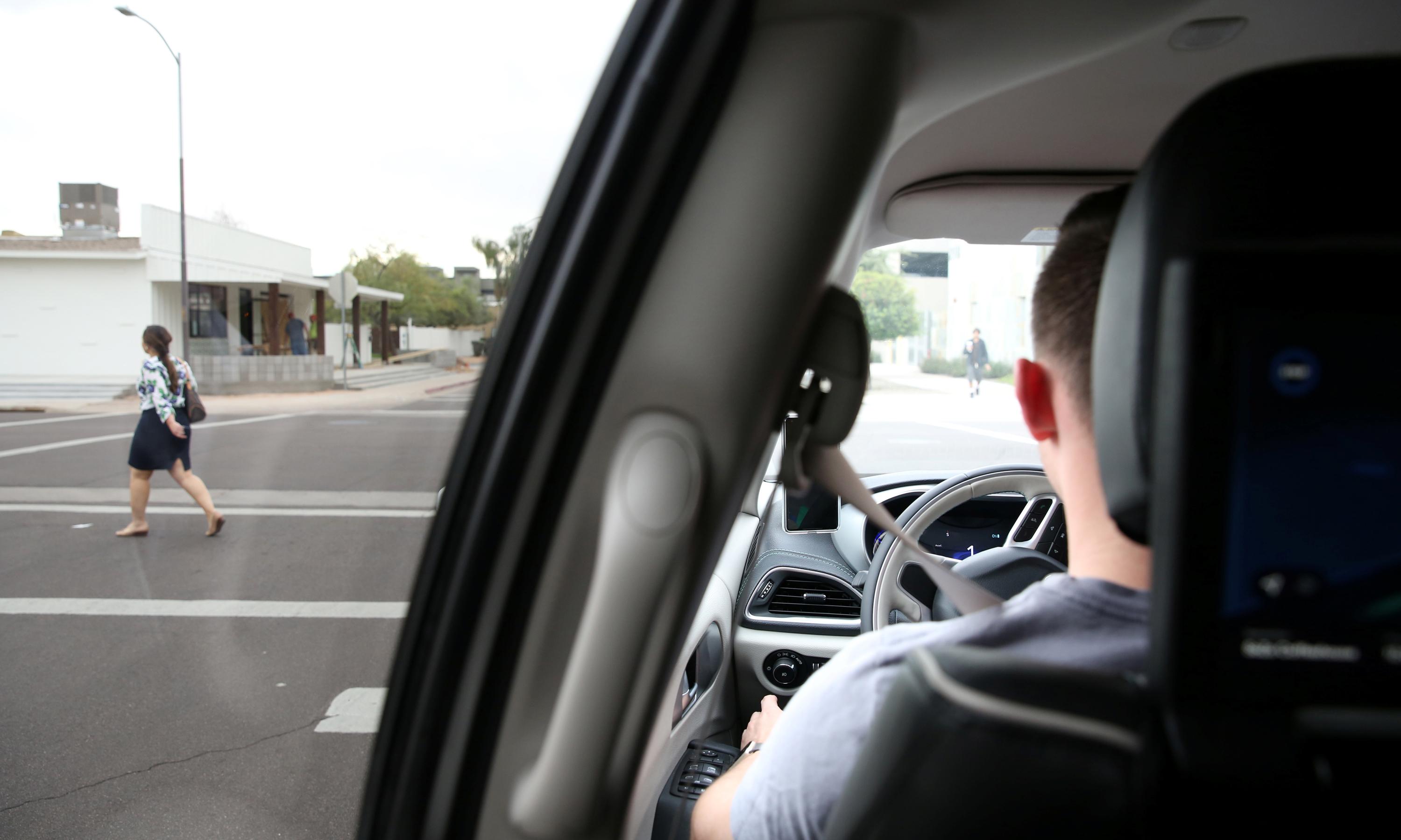 A person in the driver's seat of an autonomous vehicles looks at a pedestrian on a crosswalk.
