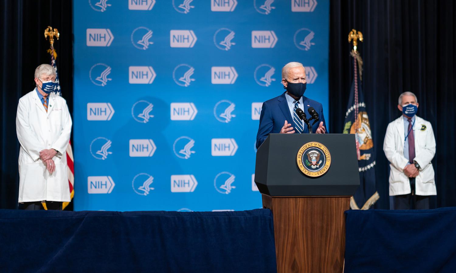 President Biden speaking at the National Institutes of Health headquarters in Bethesda, MD, flanked by NIH director Dr. Francis Collins and Dr. Anthony Fauci 