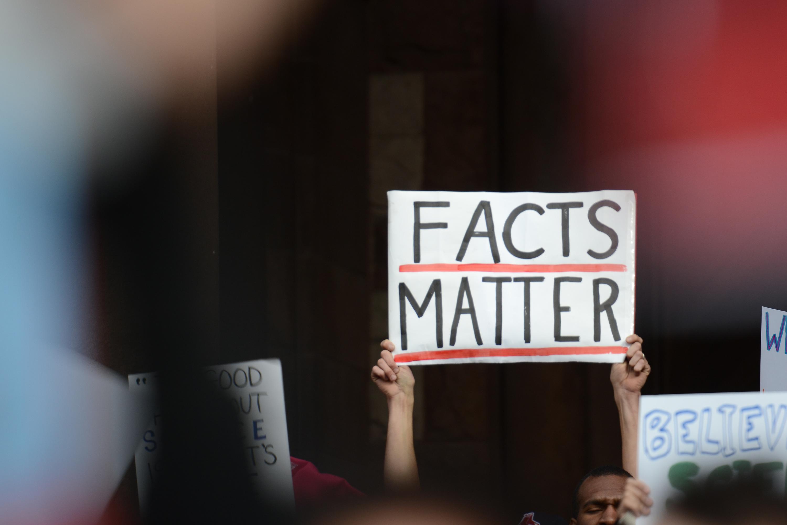 Hands holding up a sign that reads facts matter