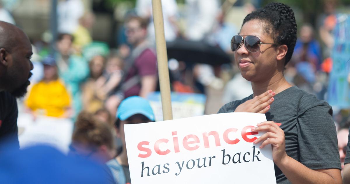Person holding a sign that says "Science has your back"
