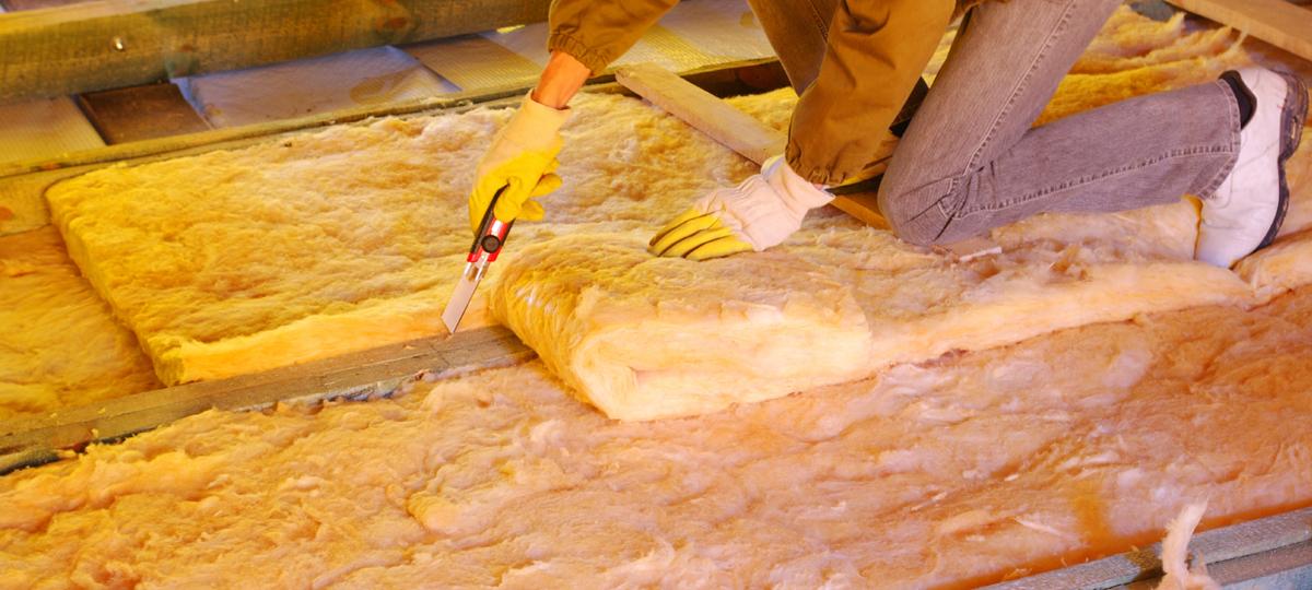 Person cutting insulation material in an attic.