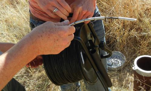 Two groundwater professionals use a device to measure depth-to-groundwater