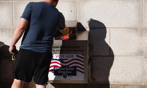 A voter sliding their ballot into a drop box.