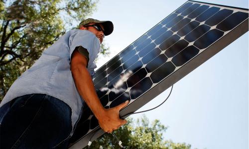 Person with hat and glasses hoisting up a solar panel