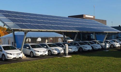 Cars lined up underneath a solar panel.